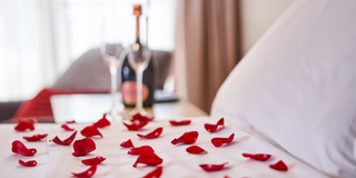 Rose petals on bed two glasses and champagne  bottle in the background 