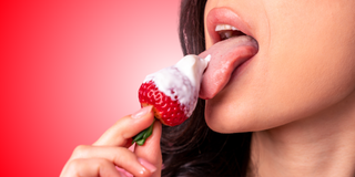 Girl licking strawberry with whip cream 